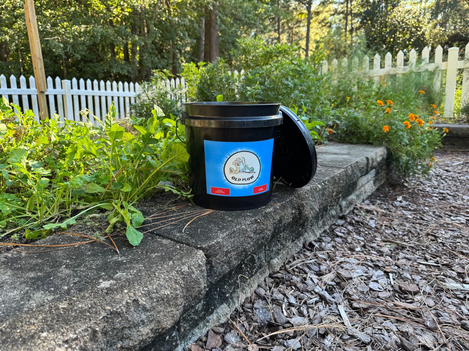 Black Old Plow bucket with blue label sitting on a stone garden wall
